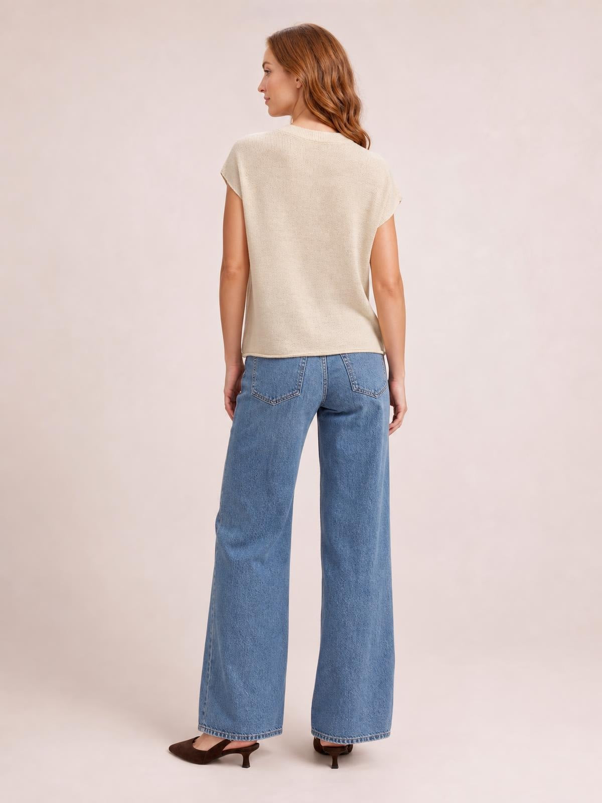 A model stands facing away in a cream exposed-seam round-neck short-sleeve sweater with a relaxed, straight silhouette and softly curved hem.