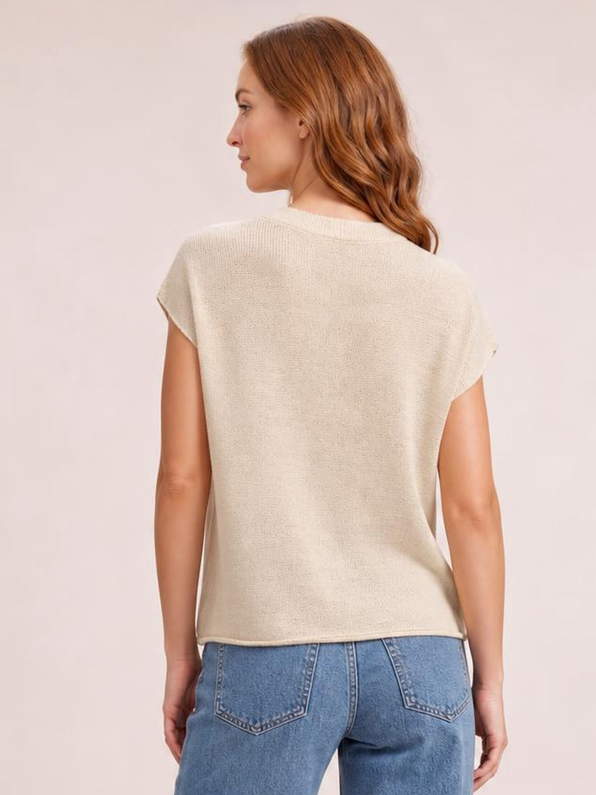 Model shown from the back wearing a cream exposed-seam round-neck short-sleeve sweater with a relaxed, straight silhouette and ribbed neckline.