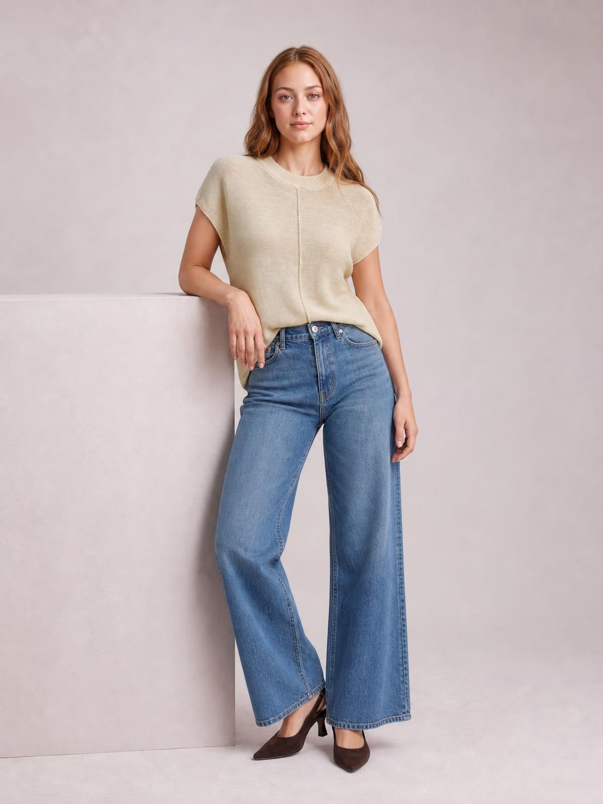 Model wearing a cream exposed seam round neck short sleeve sweater with a relaxed silhouette, standing with one arm resting on a ledge.