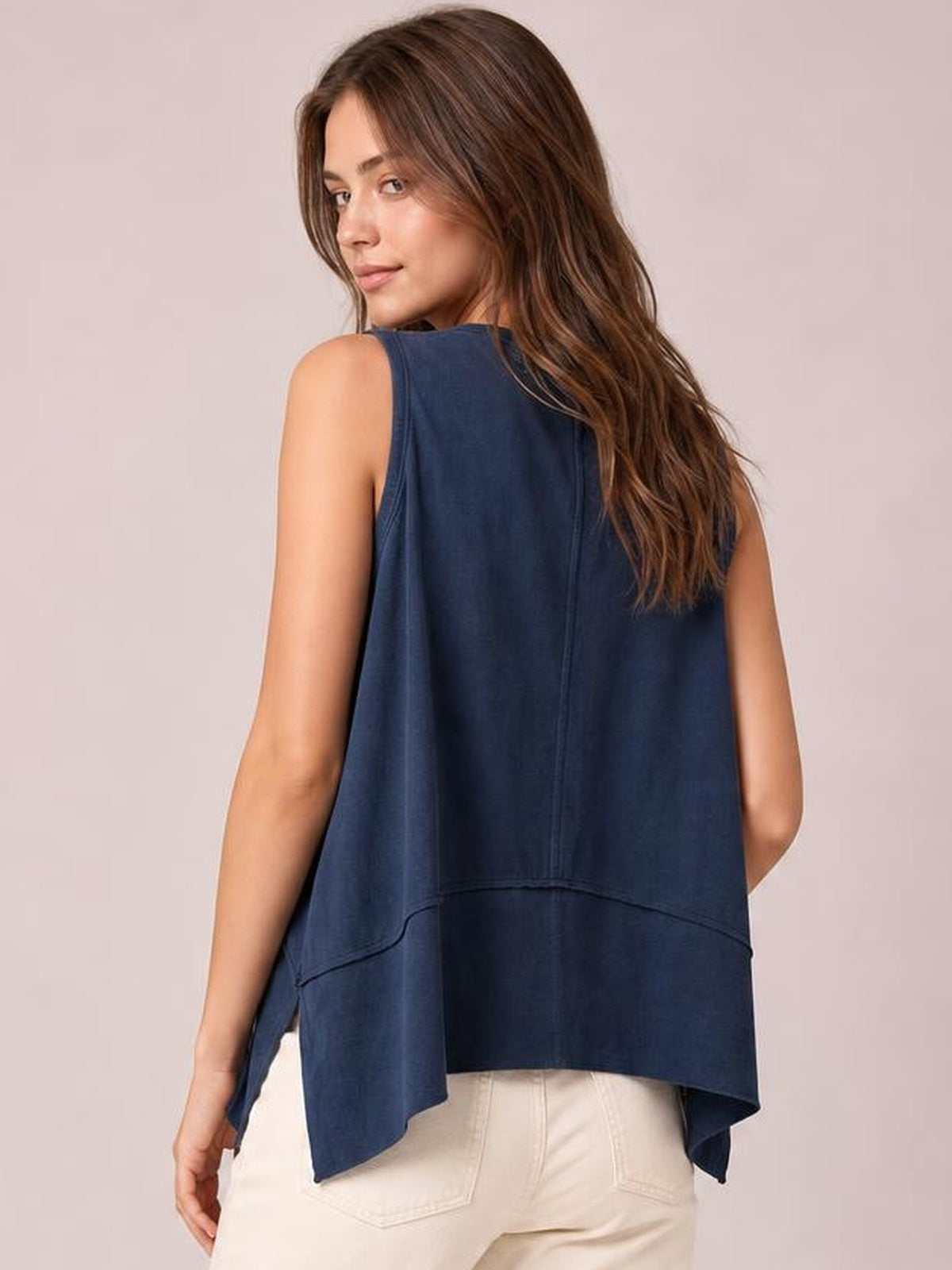 Model shows the back of a navy round-neck tank with exposed center seams, a loose flowing silhouette, and side slits creating an uneven hem.