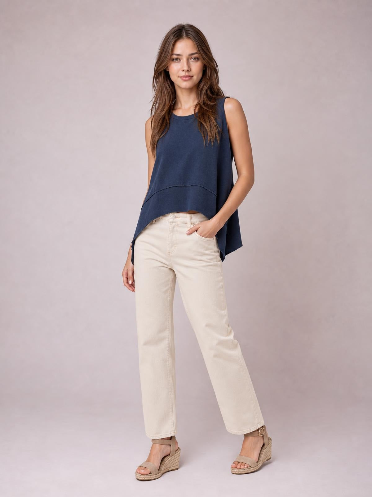 A model stands with one hand in her pocket wearing a navy round-neck tank with exposed seams, side slits, and a relaxed, swingy silhouette.