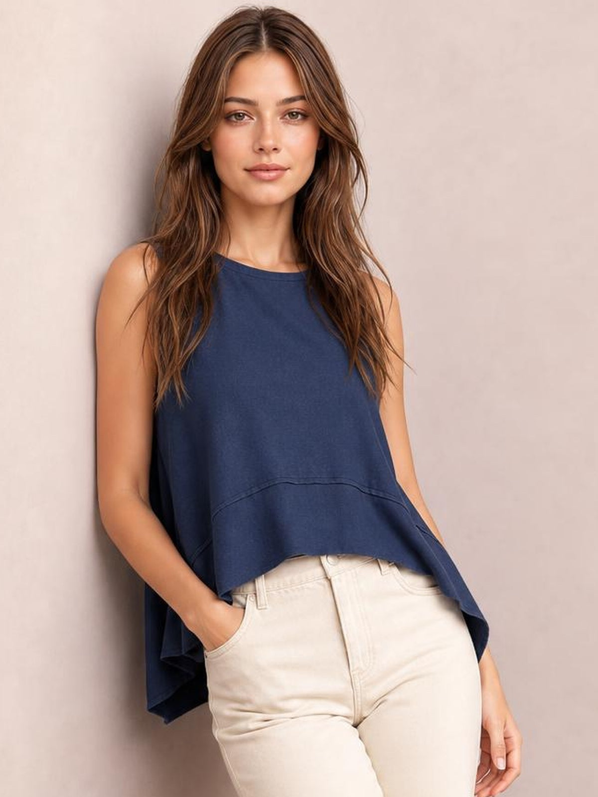 Model wearing a navy round-neck tank with exposed seams, a relaxed silhouette, and side slits, posed with one hand in a pocket.
