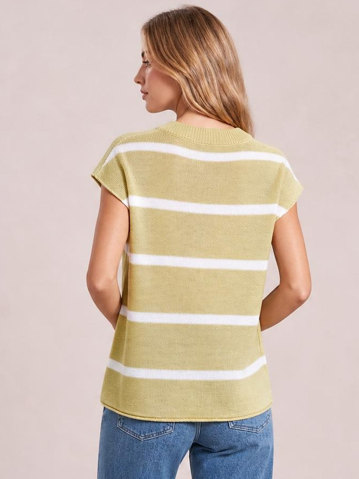 A model poses from the back in an olive green striped knit top with a round neck, short sleeves, relaxed silhouette, and visible exposed seam construction.