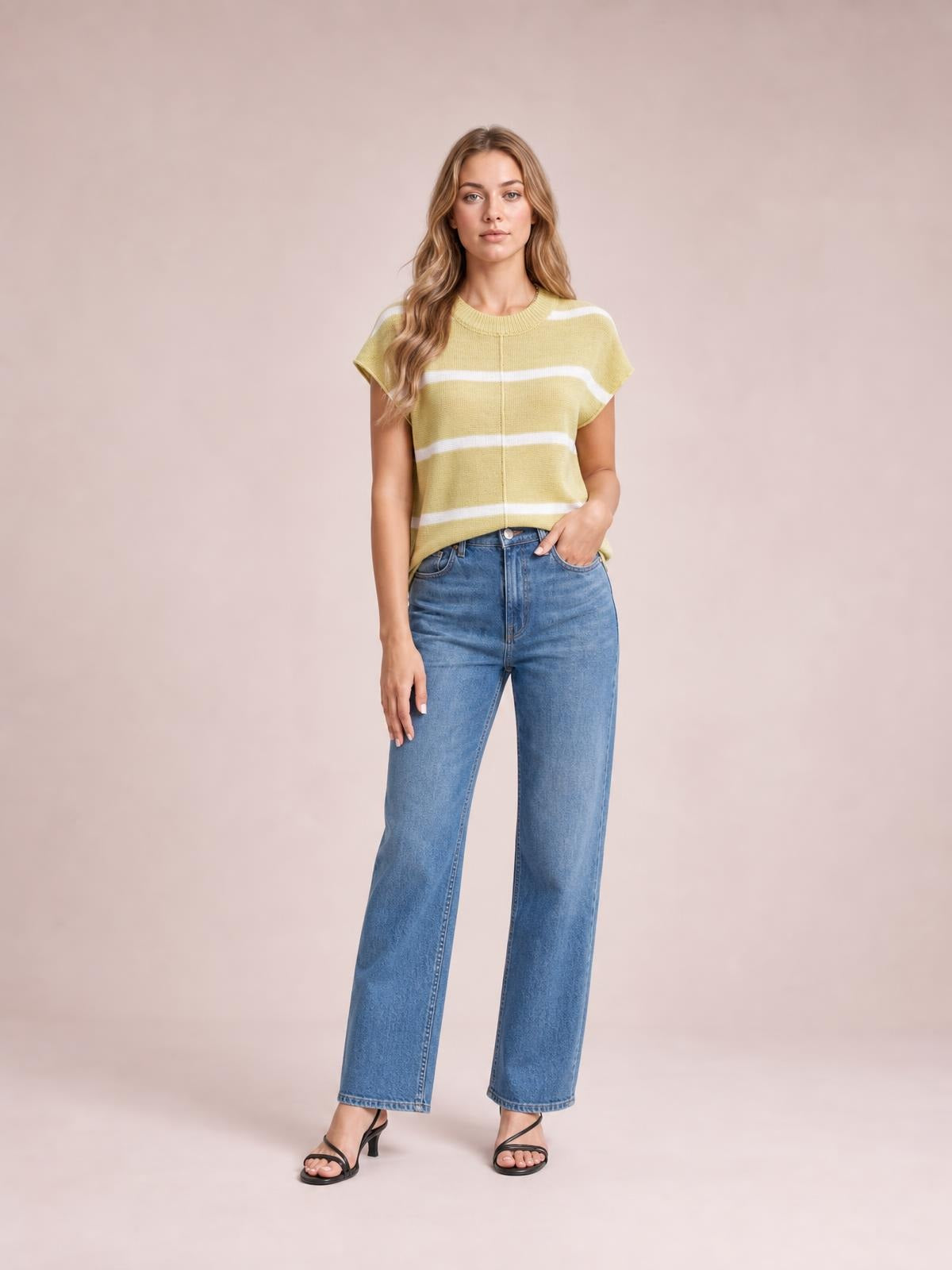 A model wears a pale yellow striped round-neck knit top with exposed center seam, short sleeves, and a relaxed silhouette, posing with one hand in her jeans pocket.
