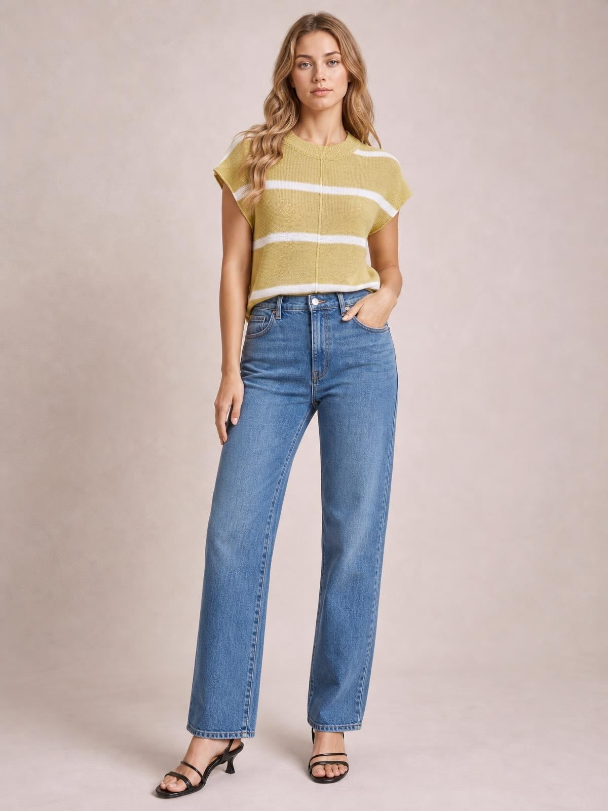 Model wears a mustard yellow striped round neck knit top with short sleeves, an exposed center seam, and a relaxed silhouette while posing with one hand in her jeans pocket.