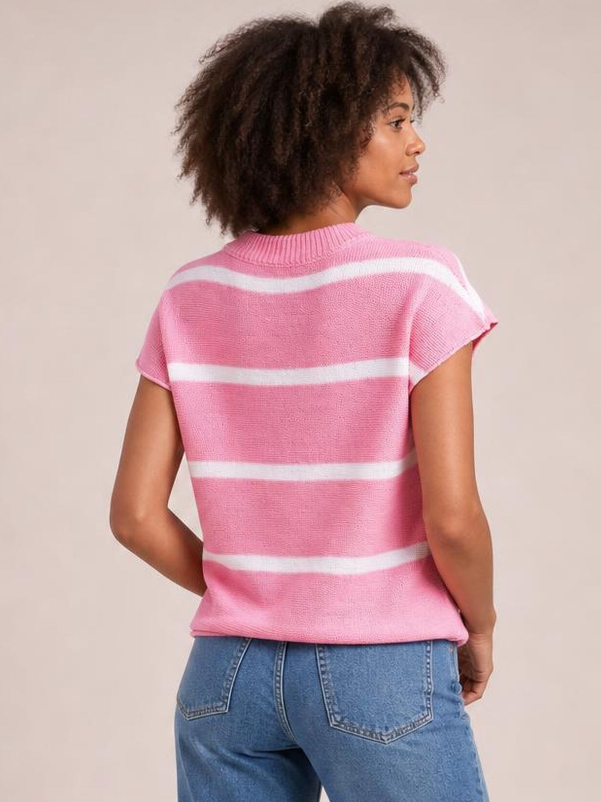 Model shown from the back in a pink knit top with white horizontal stripes, ribbed round neck, short sleeves, and visible exposed seams.