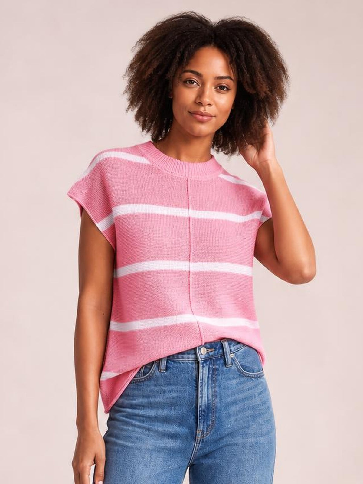 Model wearing a pink striped round neck knit top with exposed center seam, short sleeves, and a relaxed straight silhouette, posing with one hand in her hair.