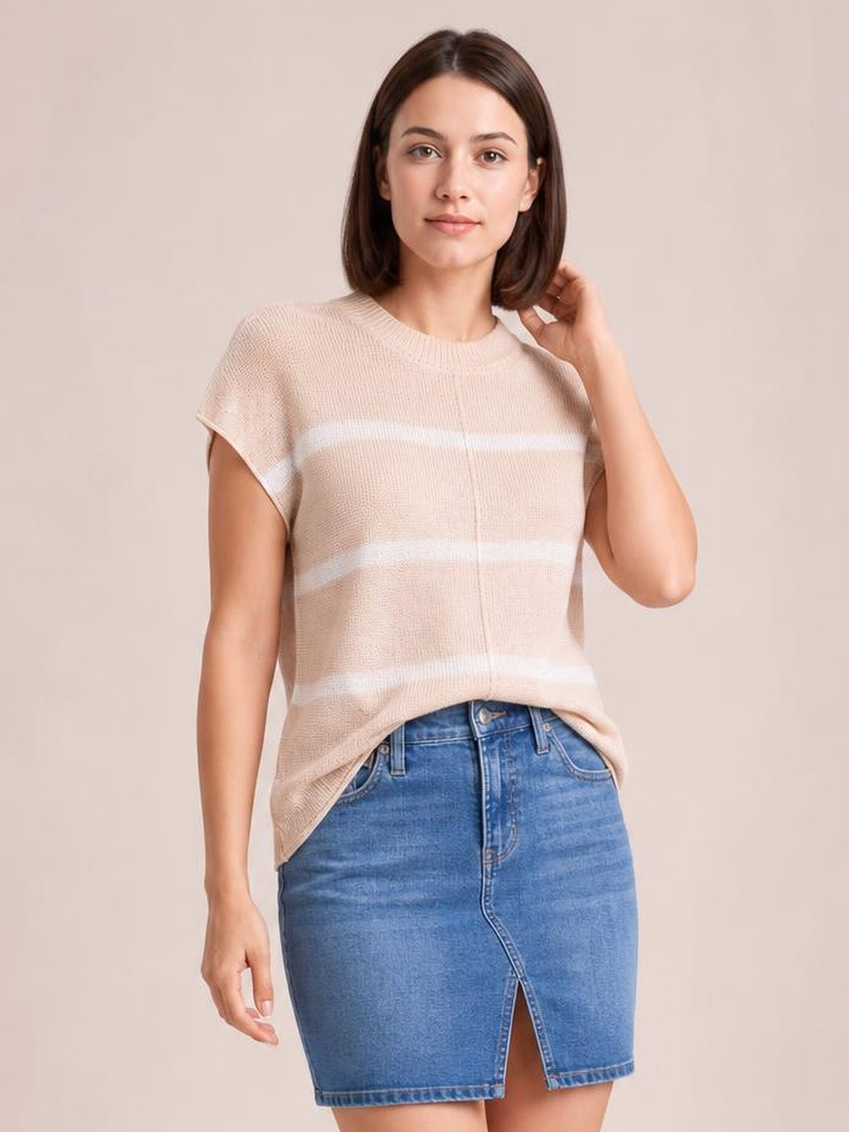 Model poses with one hand to her hair, wearing a beige striped knit top with a round neck, short sleeves, relaxed silhouette, and visible exposed center seam.