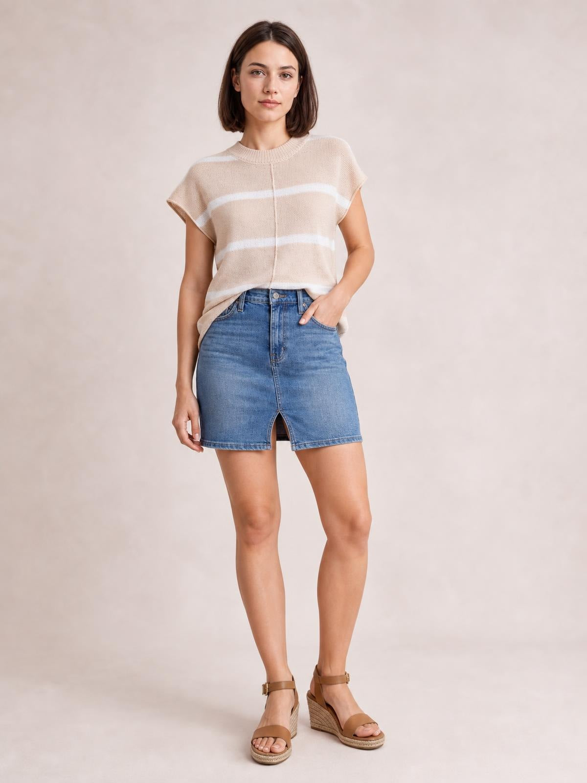 Model poses in a beige striped round neck knit top with exposed center seam, short sleeves, and a relaxed silhouette.