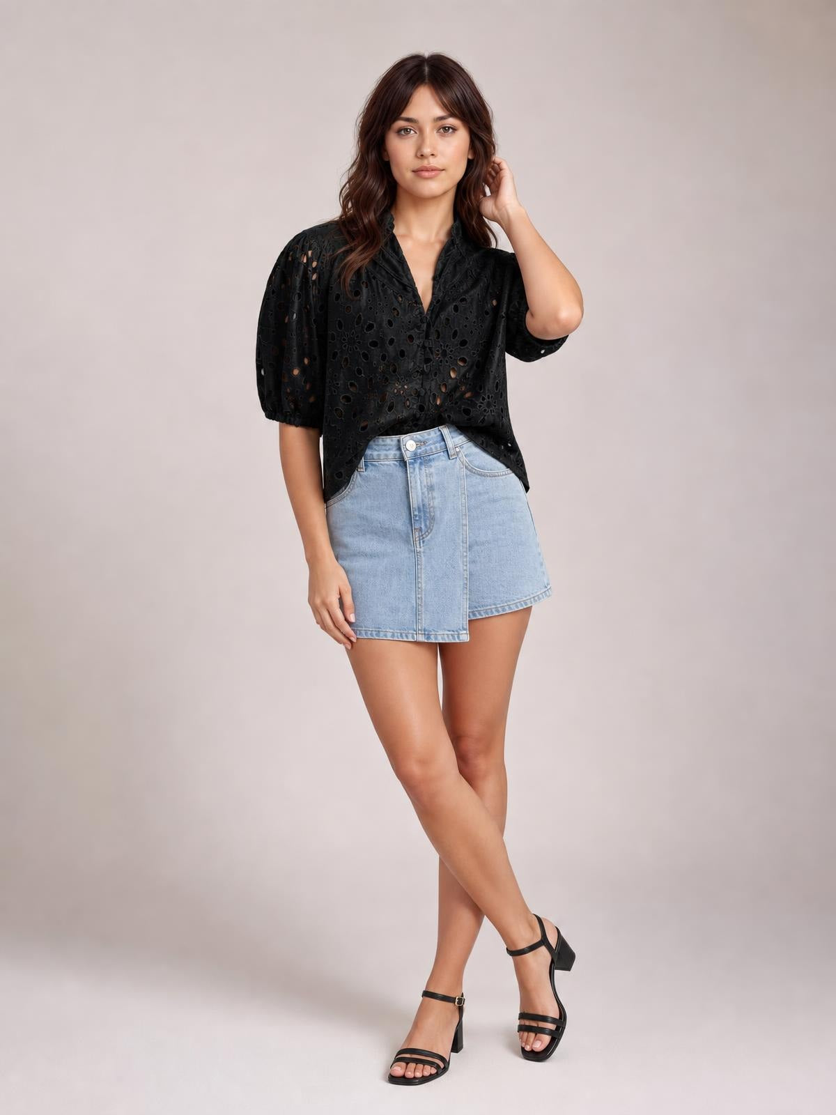 Model poses with crossed legs and one hand in her hair, wearing a black eyelet button-up blouse with half sleeves and a relaxed silhouette.