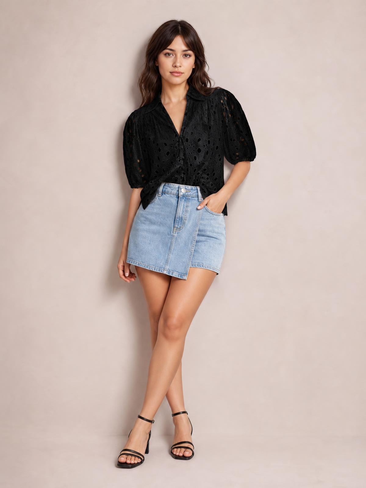 Model poses with one hand in her pocket wearing a black eyelet button-up blouse with a collared neckline, puffed half sleeves, and a relaxed silhouette.