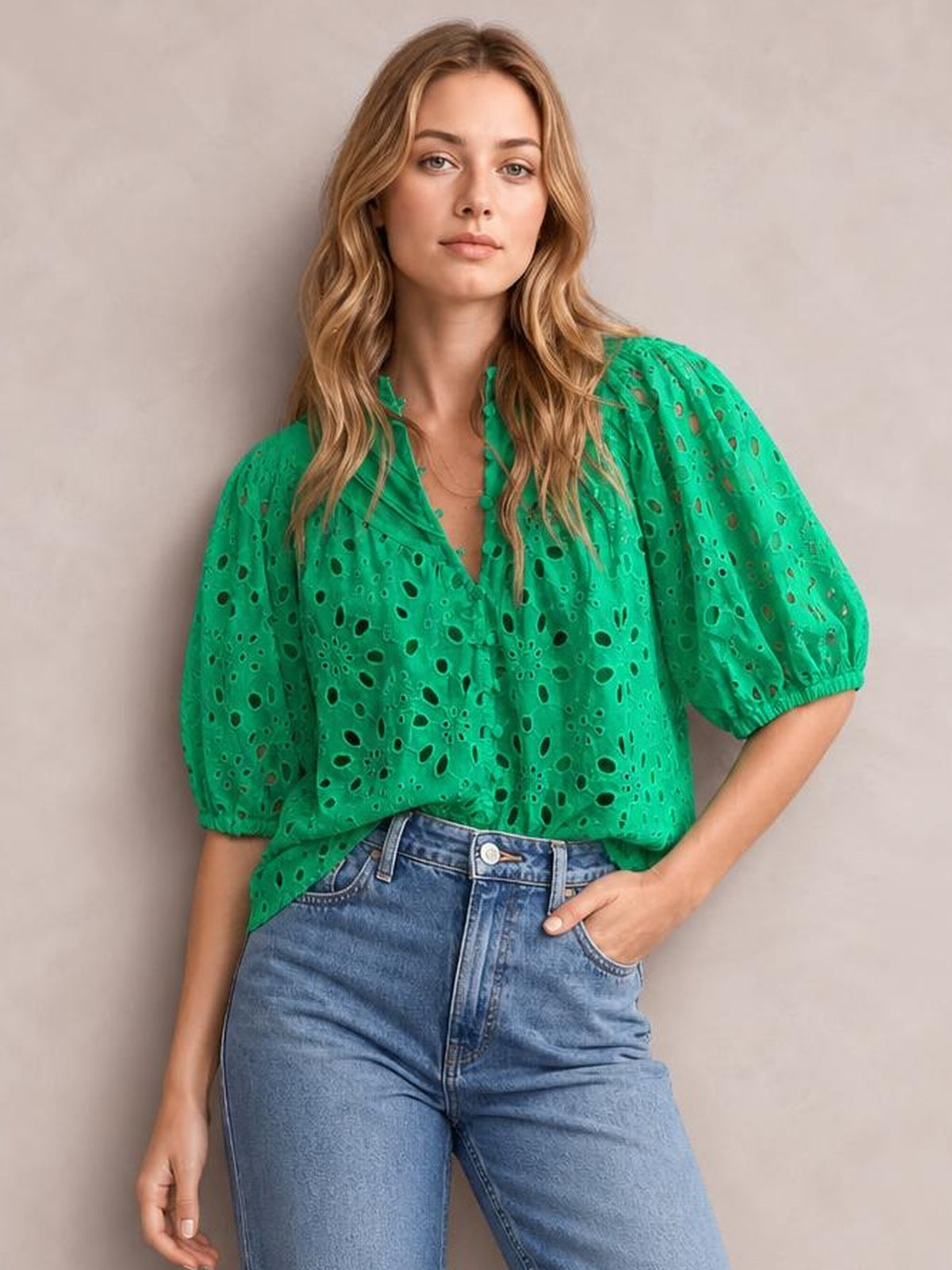 A model poses in a bright green eyelet button-up blouse with puffed half sleeves, elastic cuffs, a relaxed silhouette, and blue jeans.
