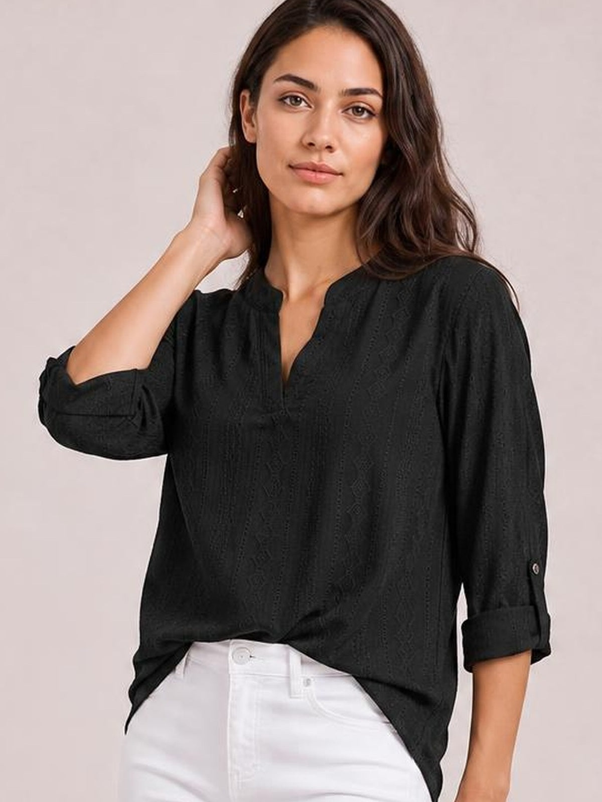 A model poses in a black eyelet top with a notched neckline, roll-tab three-quarter sleeves, and a relaxed silhouette, lifting one hand to her hair.