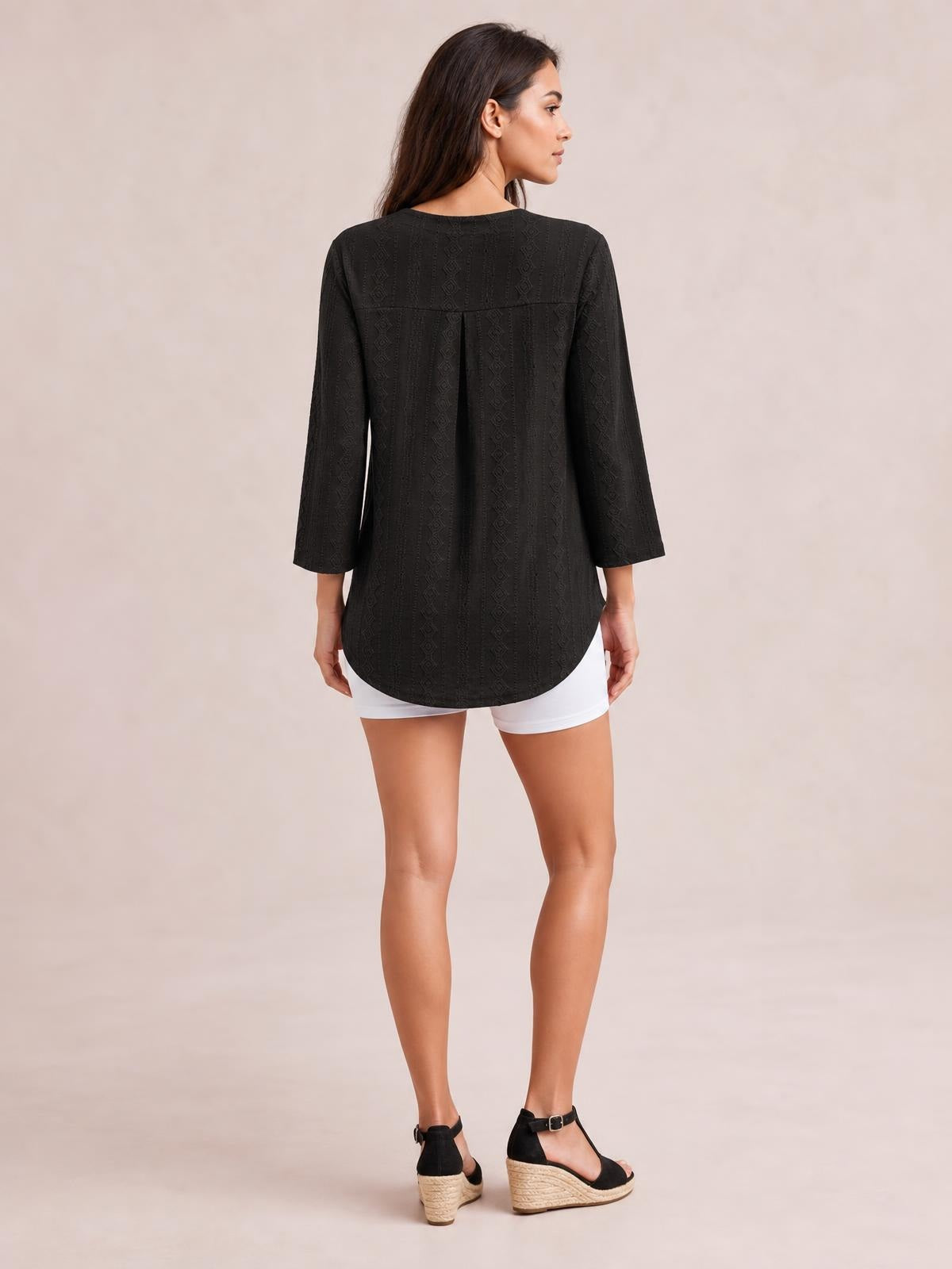 Model shown from behind wearing a black eyelet top with three-quarter sleeves, a back yoke, relaxed silhouette, and curved hem.