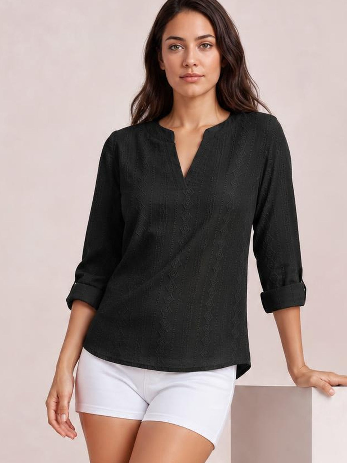 Model poses in a black eyelet top with a notched neckline, relaxed straight silhouette, and rolled tab sleeves over white shorts.