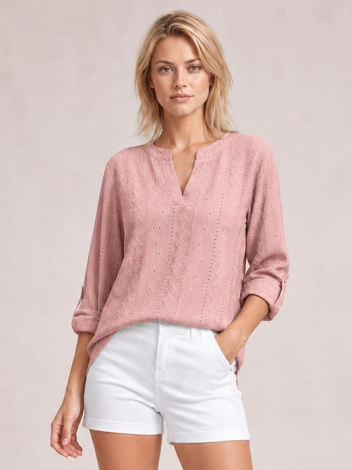 Model wears a dusty pink eyelet top with a notched neckline, relaxed silhouette, and long roll-tab sleeves styled rolled up while standing with one hand in her pocket.