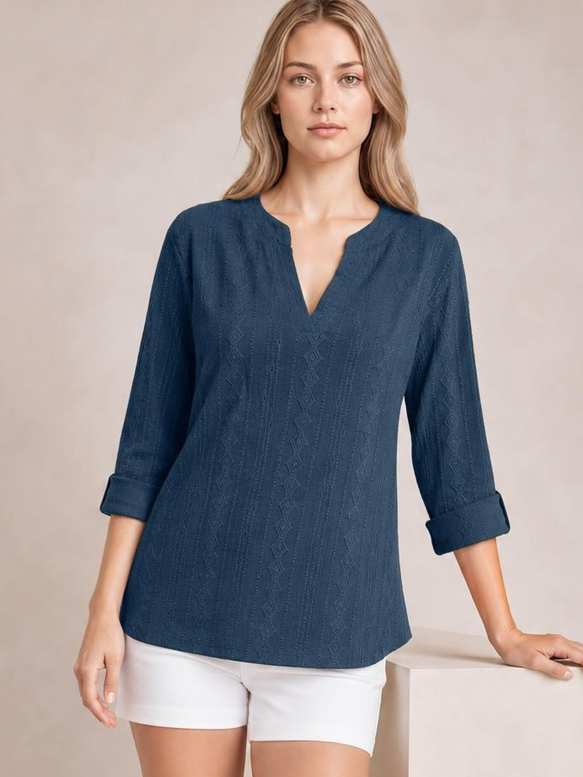Model wears a navy eyelet top with a notched neckline, relaxed straight silhouette, and long sleeves rolled to the forearms with tab details.