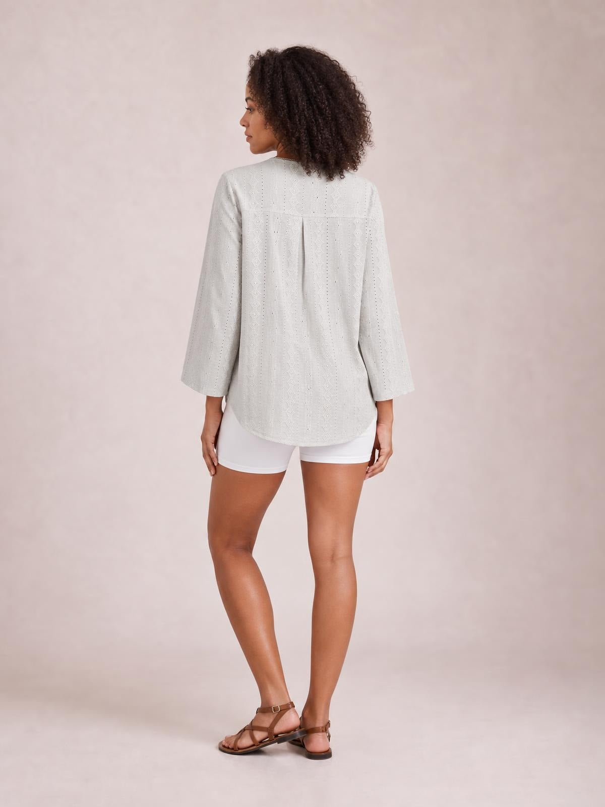 A model poses from behind in a light gray eyelet shirt with a relaxed silhouette, three-quarter sleeves, back yoke, center pleat, and curved hem.