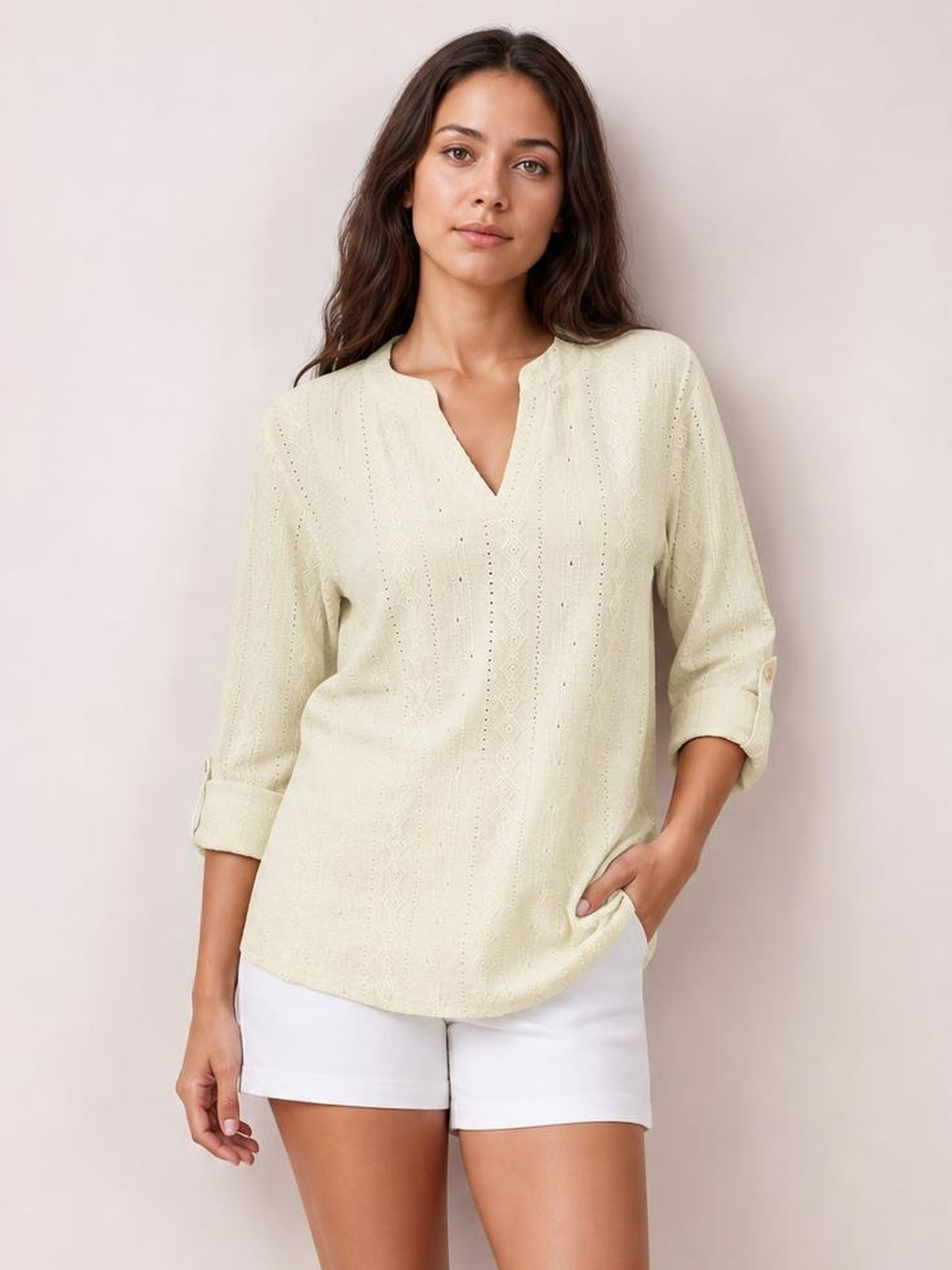 A model stands in an ivory eyelet top with a notched neckline, relaxed silhouette, and long roll-tab sleeves, paired with white shorts.