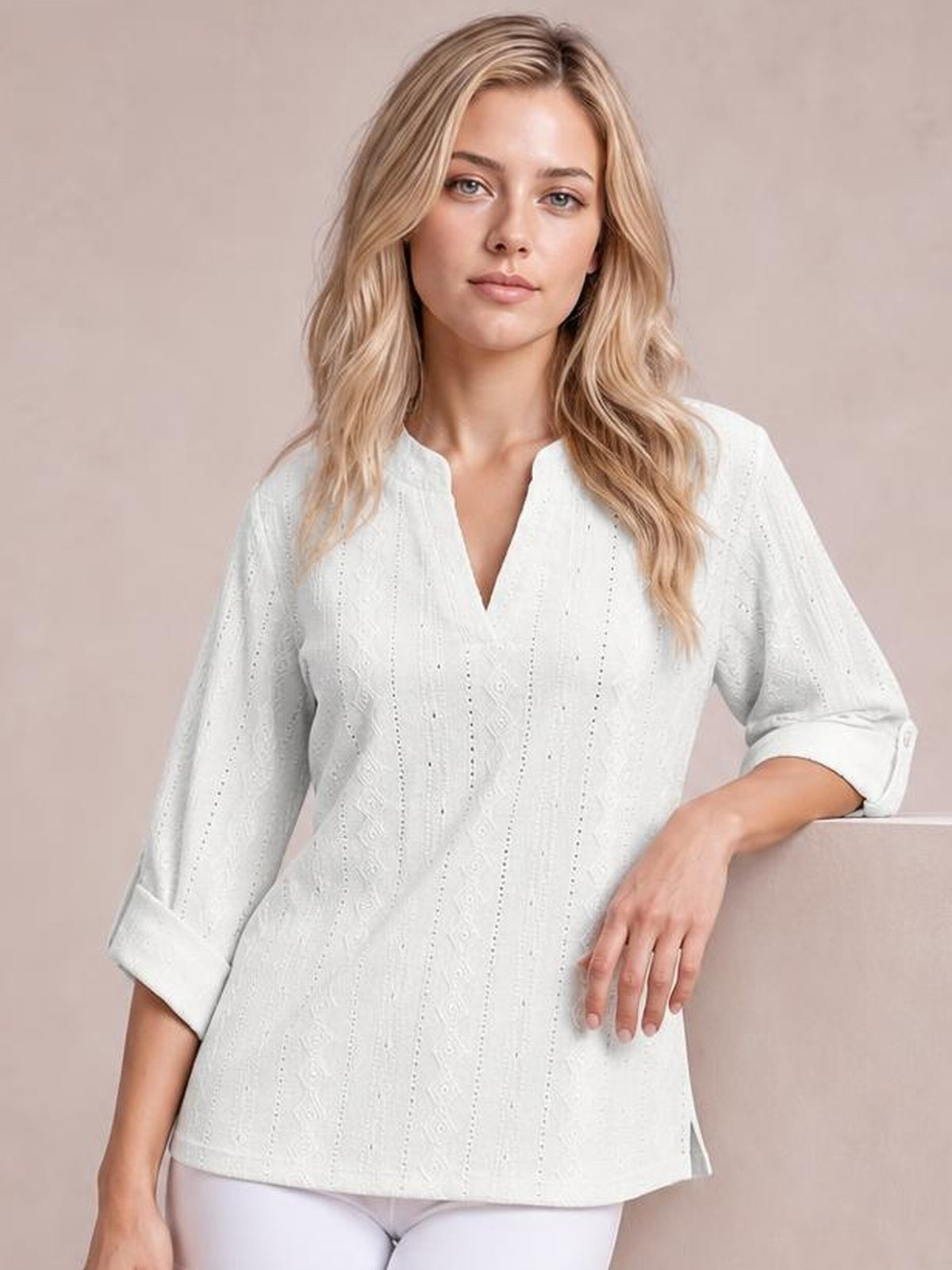 A model wears a white eyelet top with a notched neckline, three-quarter roll-tab sleeves, and a relaxed straight silhouette while leaning casually.
