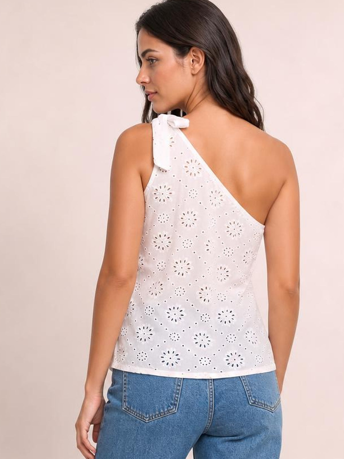 Model shown from behind wearing a white eyelet one-shoulder tank with a tied shoulder detail, asymmetrical neckline, and relaxed straight silhouette.