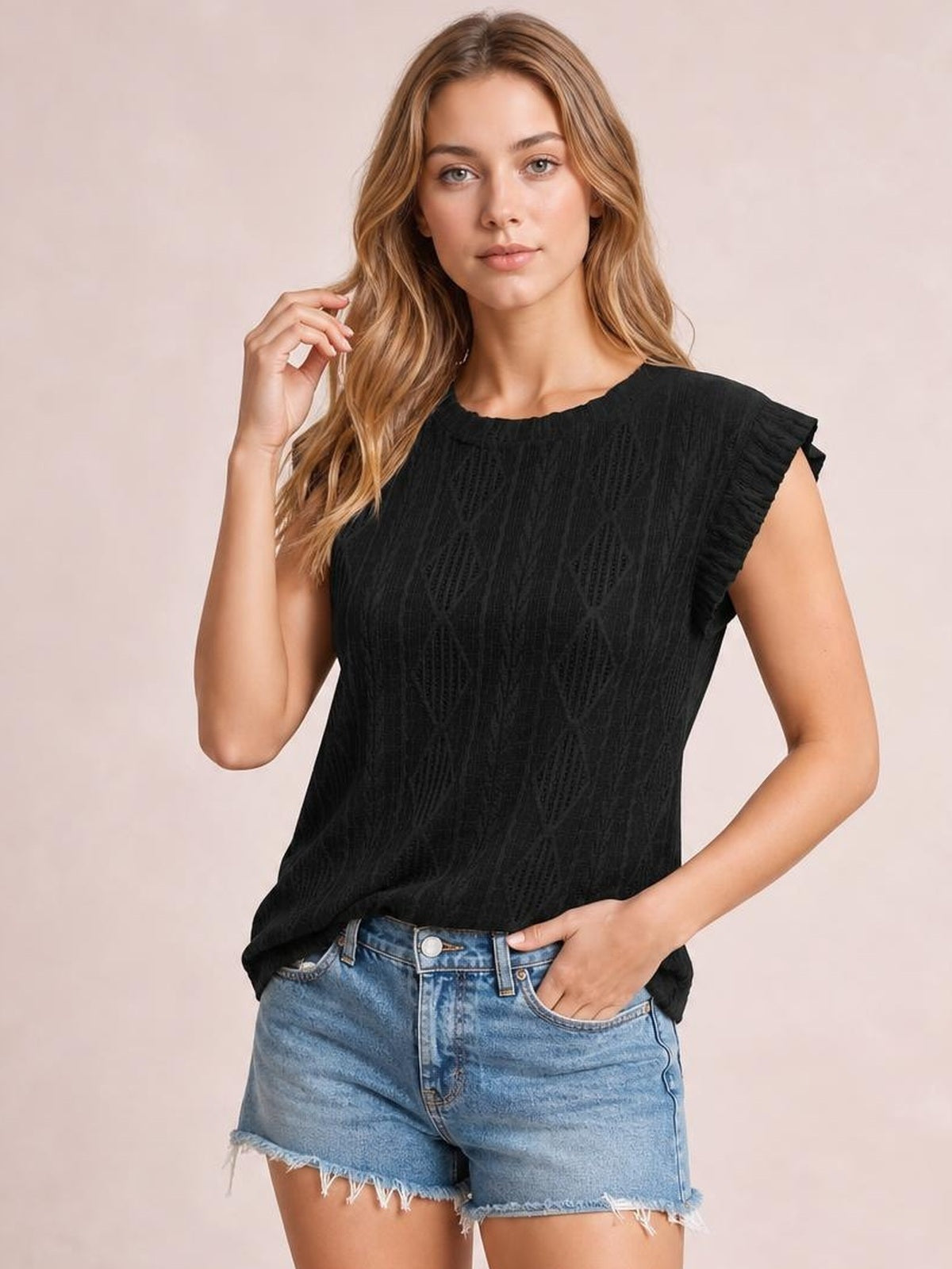 Model wears a black opaque eyelet top with a round neck, cap sleeves, textured detailing, and a relaxed silhouette while posing with one hand in her pocket.