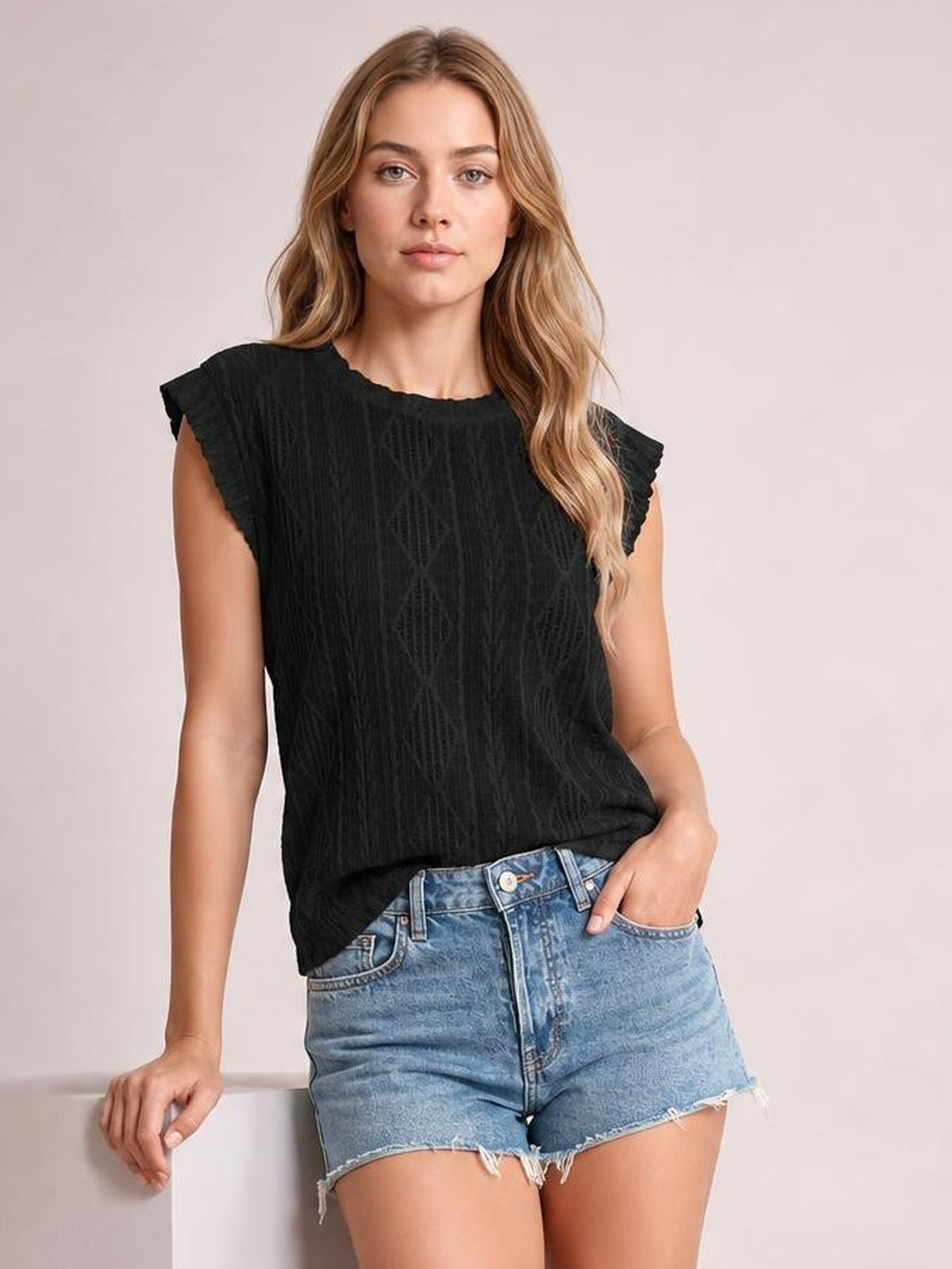 A model wears a black eyelet round-neck cap-sleeve top with a relaxed straight silhouette, gently textured construction, and a loose untucked hem.