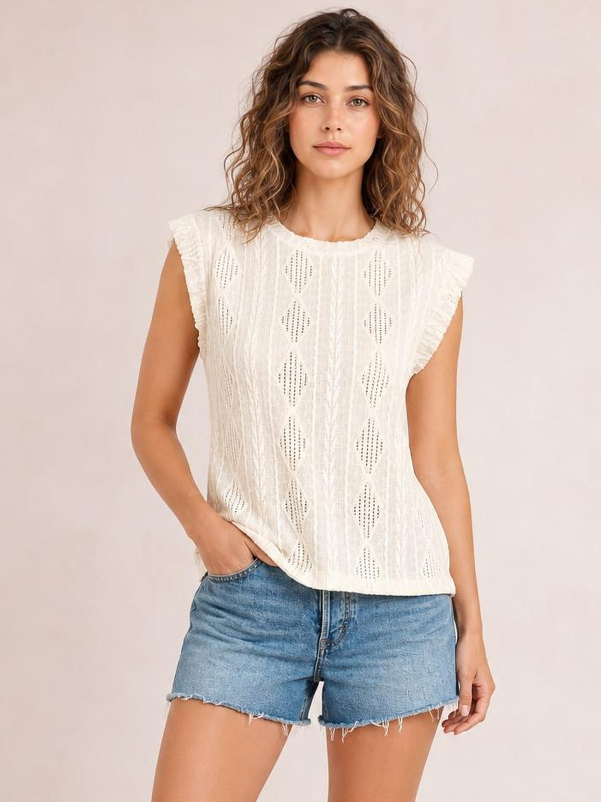 Model poses with one hand in her pocket wearing an opaque white eyelet top with a round neck, cap sleeves, vertical textured panels, and a relaxed silhouette.