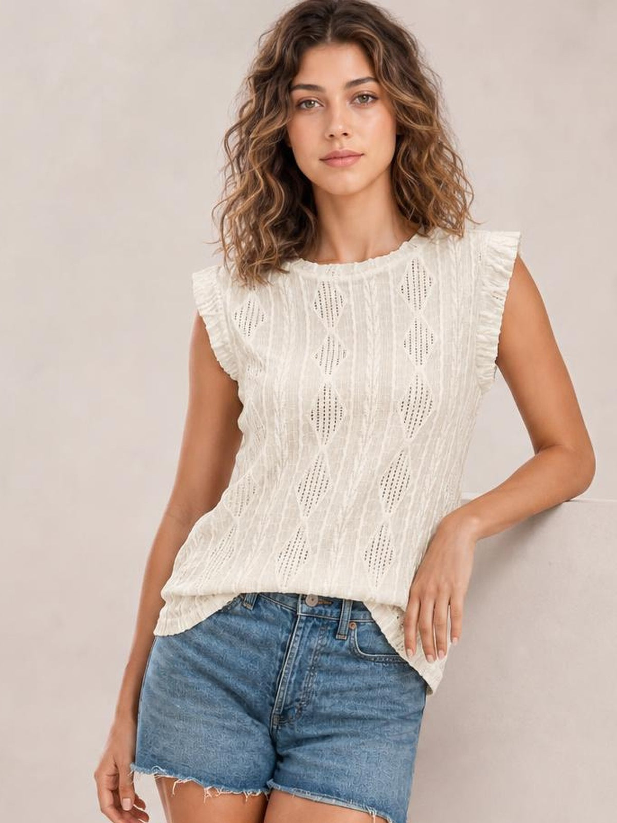 Model wears a white eyelet round-neck cap-sleeve top with ruffled shoulders, a relaxed straight silhouette, and a curved hem.