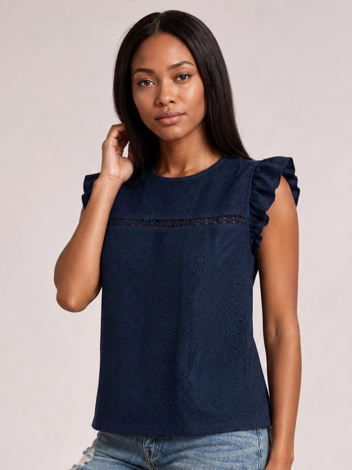 Model poses with one hand in her hair, wearing a navy eyelet top with a round neck, ruffled cap sleeves, cutout band, and straight silhouette.
