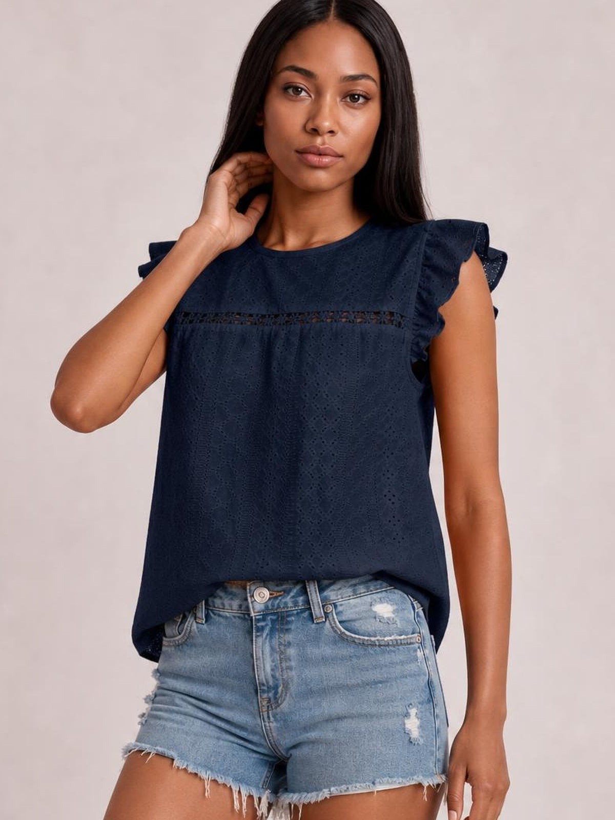 Model poses with one hand at her neck in a navy eyelet round-neck top featuring cap sleeves, cutout detailing, and a relaxed straight silhouette.