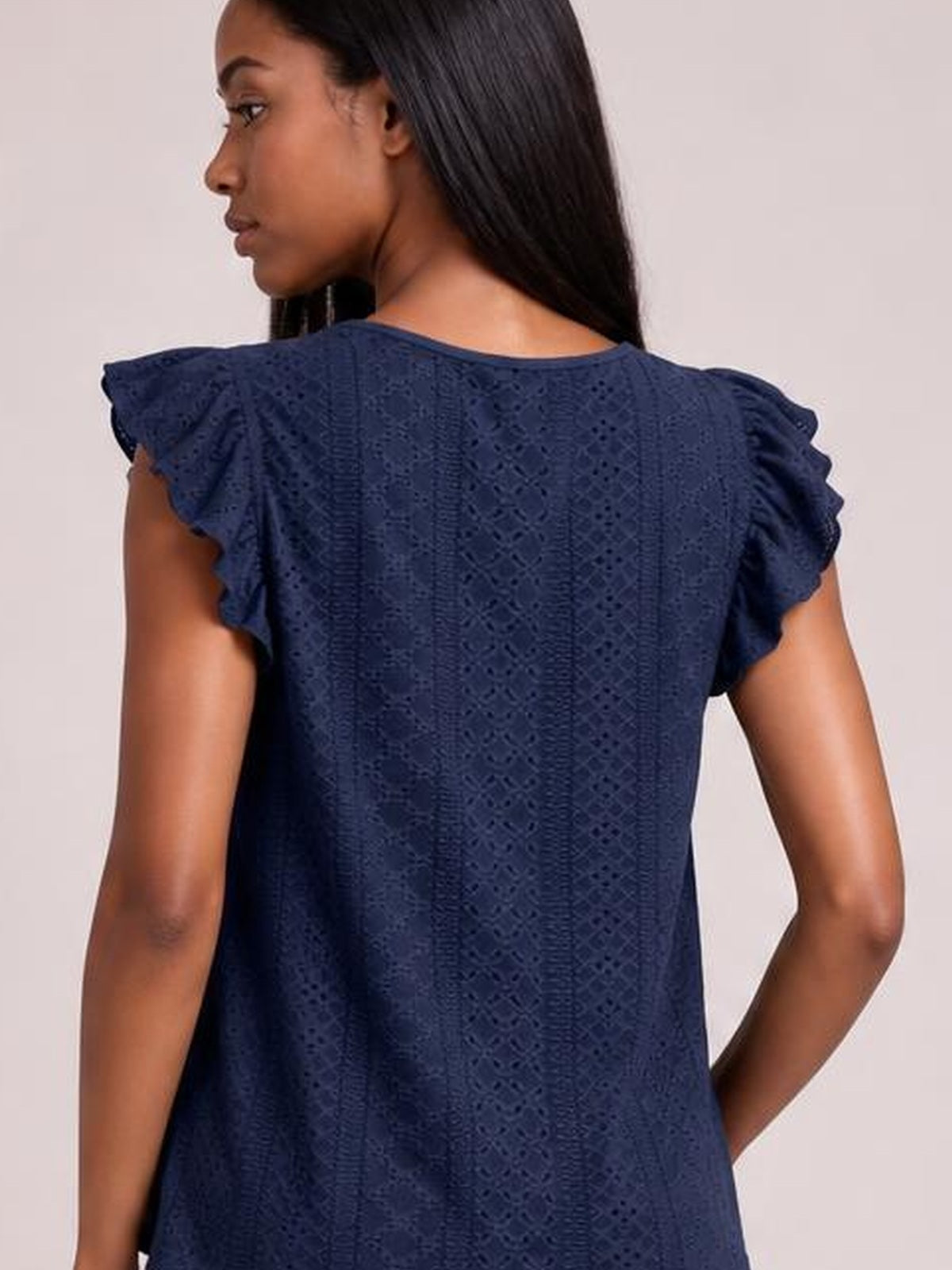 A model looks over her shoulder in a navy eyelet top with a round neck, ruffled cap sleeves, cutout texture, and a relaxed straight silhouette.