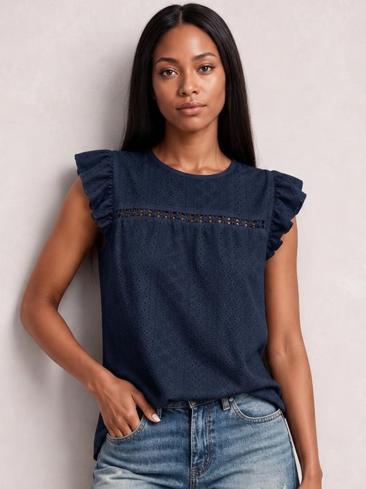 A model poses in a navy eyelet round-neck top with ruffled cap sleeves, a horizontal cutout band, and a relaxed straight silhouette.