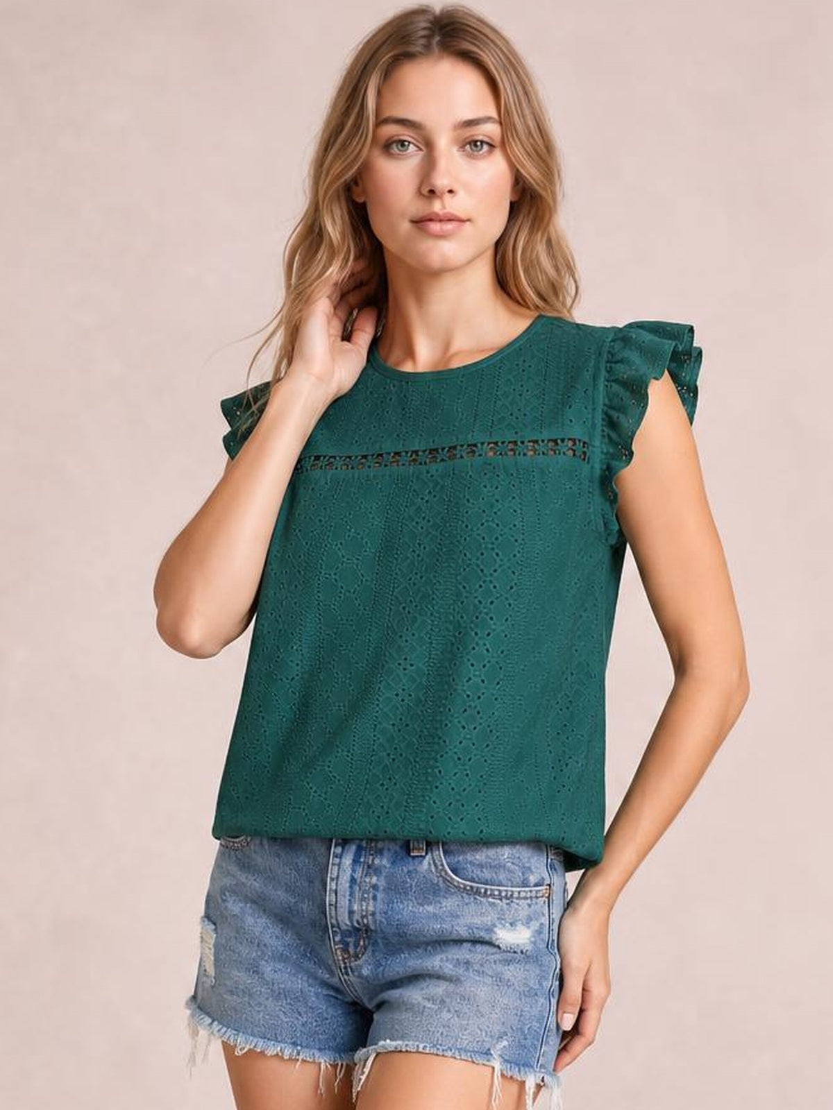 Model poses in a teal eyelet top with a round neck, cap sleeves, ruffled shoulders, horizontal cutout trim, and a relaxed straight silhouette.