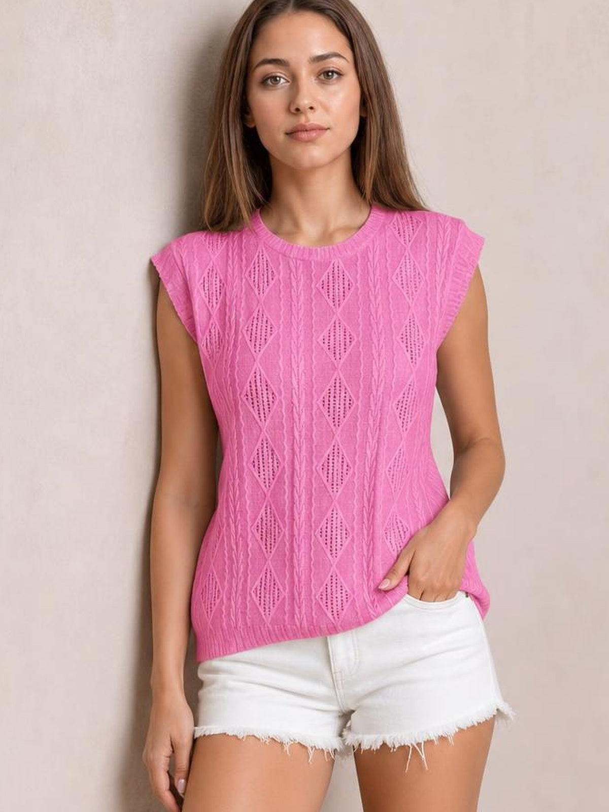 Model wears a pink eyelet round-neck cap-sleeve top with a relaxed straight silhouette, textured diamond construction, and one hand resting in her pocket.