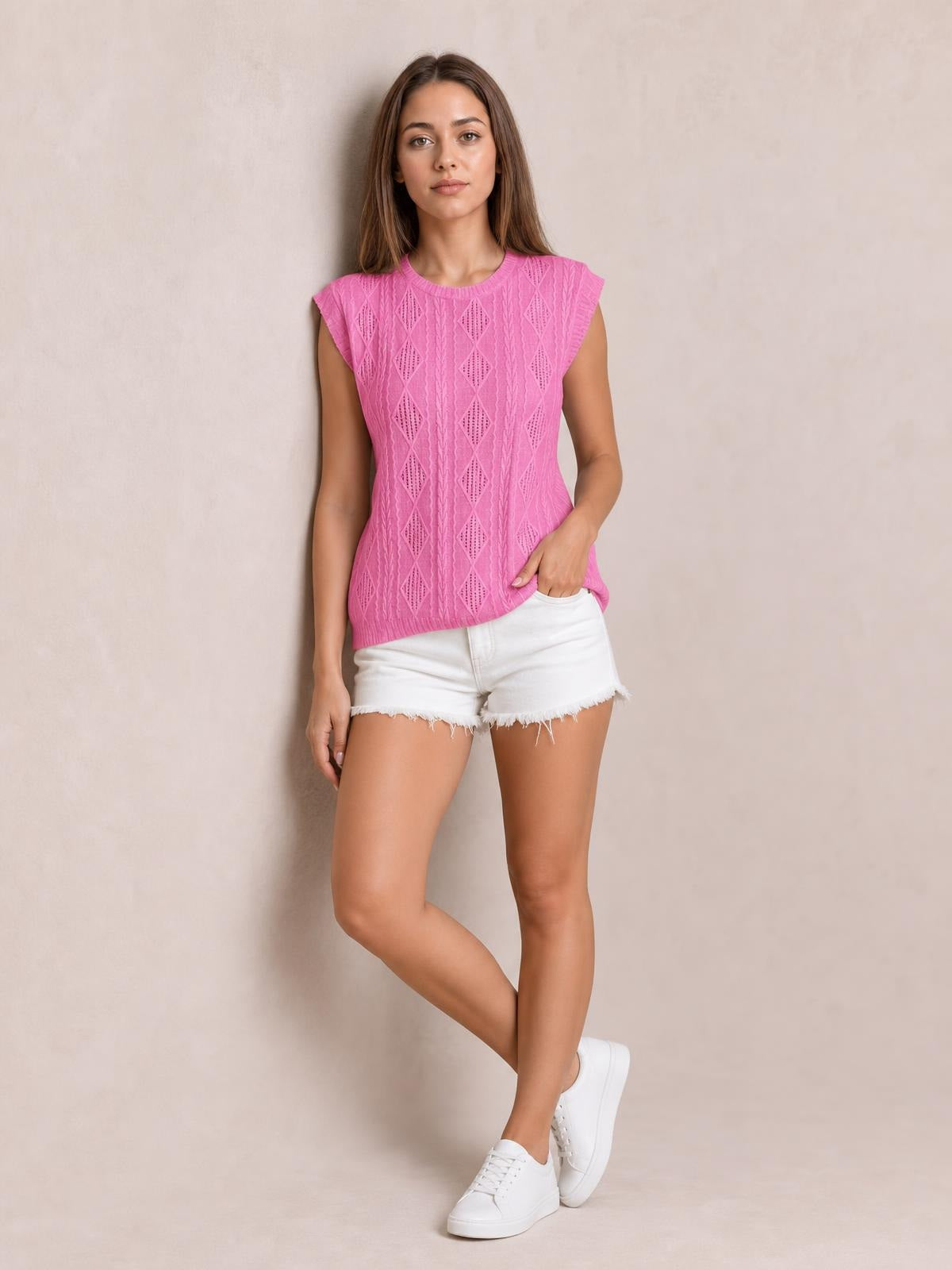 Model wearing a bright pink eyelet round-neck cap-sleeve top with a straight silhouette and textured diamond construction, paired with white denim shorts.