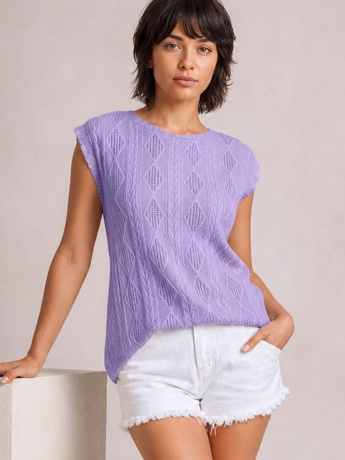 A model poses in a lavender eyelet round-neck cap-sleeve top with a relaxed silhouette, textured diamond pattern, and slightly curved hem.