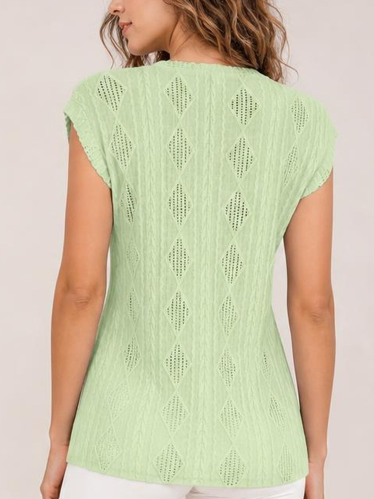 Back view of a model wearing a mint green eyelet top with a round neckline, cap sleeves, diamond-pattern cutouts, and a relaxed straight silhouette.