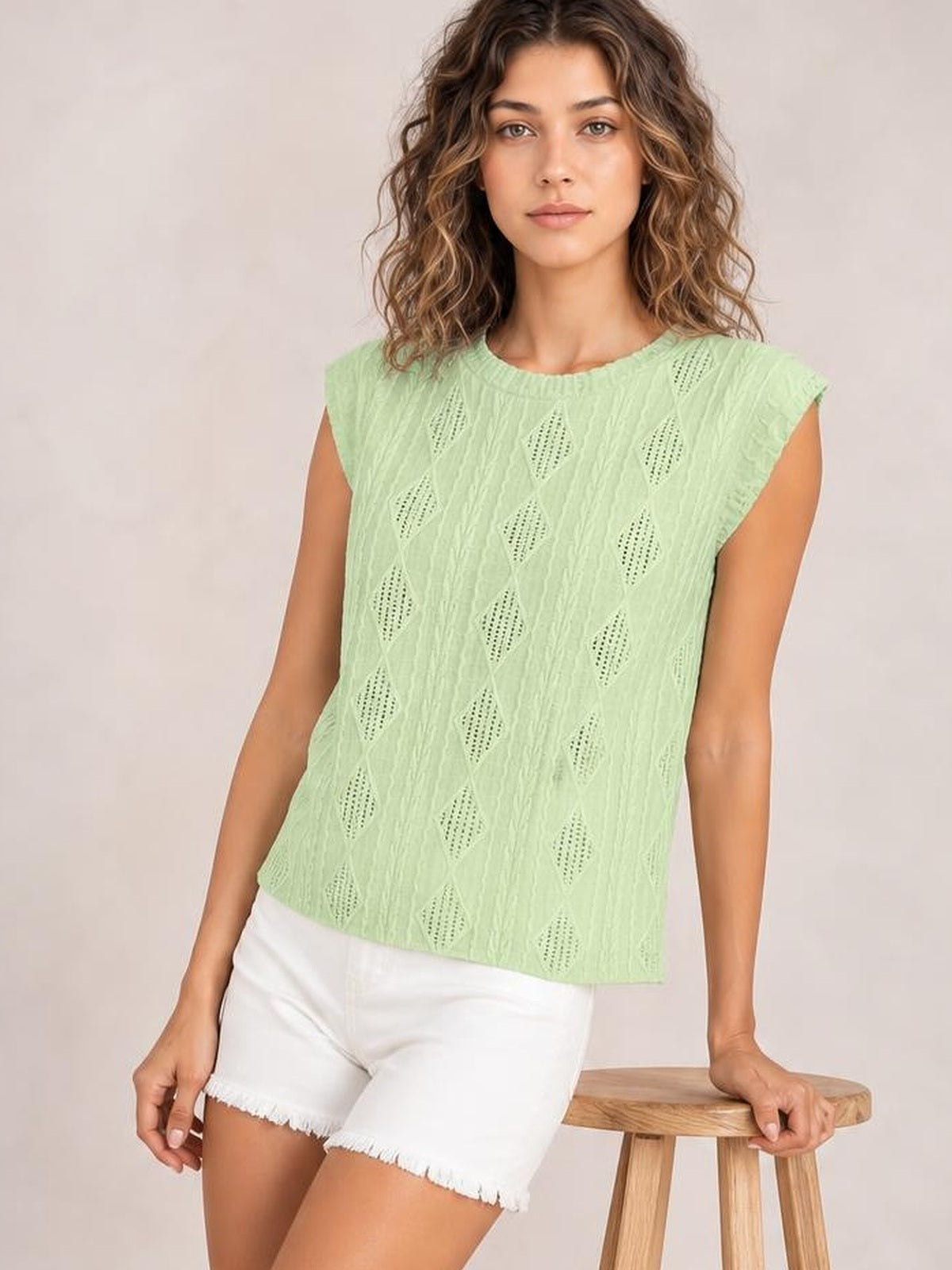 A model sits leaning on a stool in a mint green eyelet top with a round neck, cap sleeves, textured diamond cutouts, and a relaxed straight silhouette.