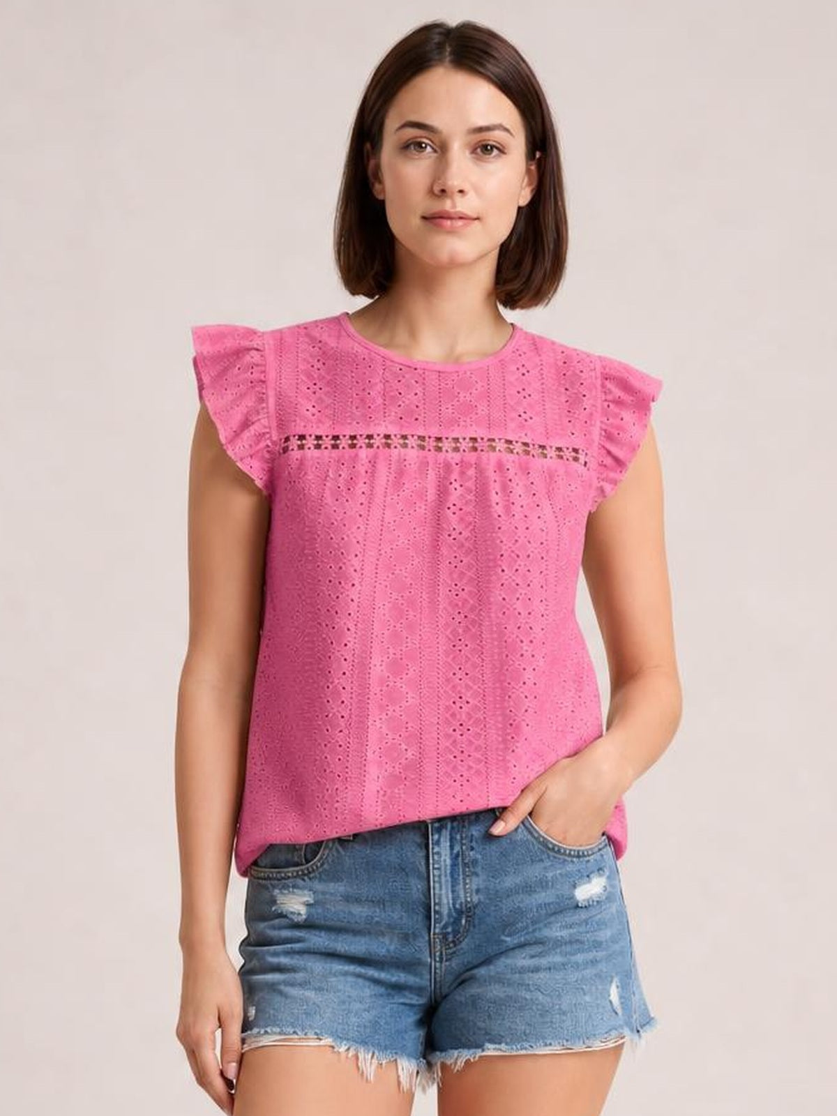A model poses in a pink eyelet round-neck cap-sleeve top with ruffled sleeves, a horizontal cutout band, and a relaxed straight silhouette.