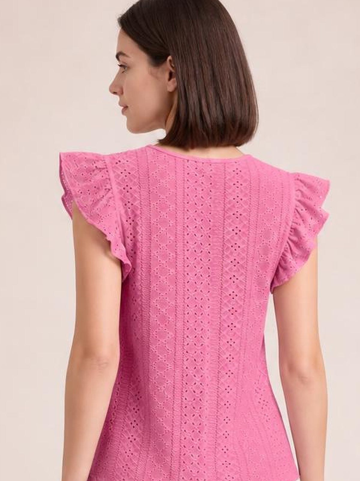 Model shown from the back wears a bright pink eyelet top with vertical cutout detailing, a round neckline, flutter cap sleeves, and a gently fitted silhouette.
