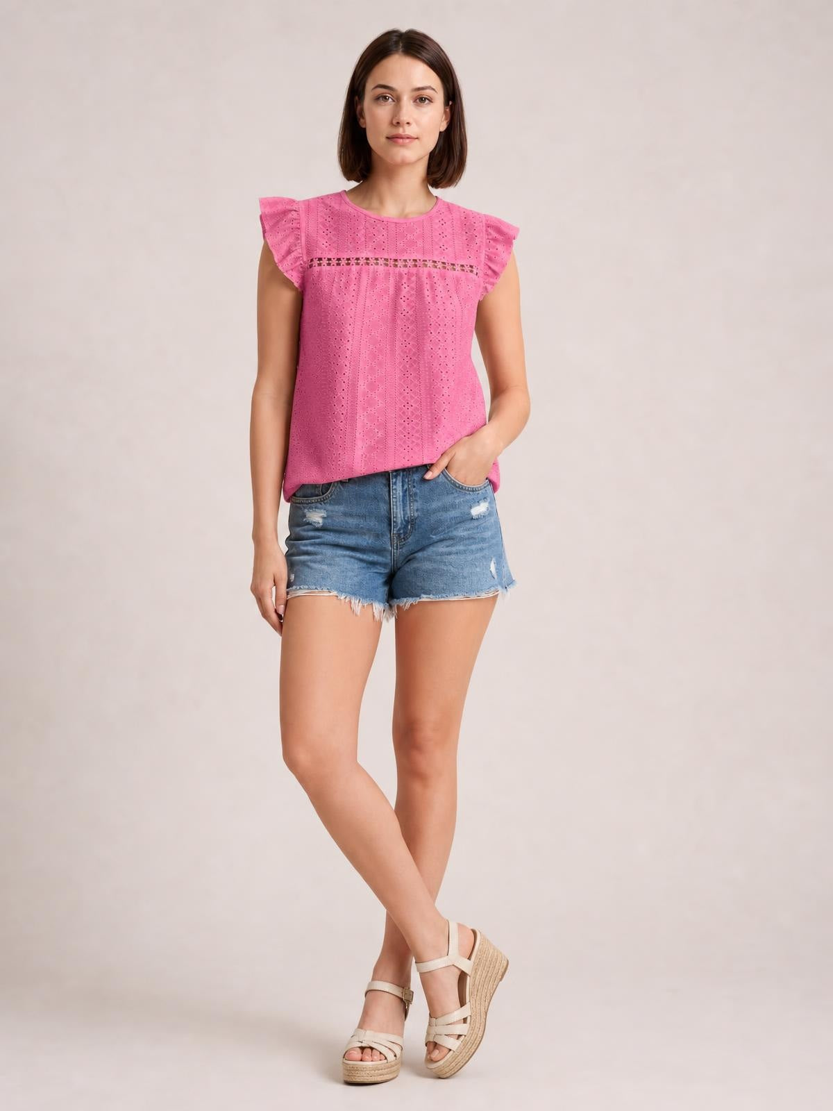 Model poses in a pink eyelet round neck cap sleeve top with cutout detailing, a relaxed silhouette, and ruffled sleeves.