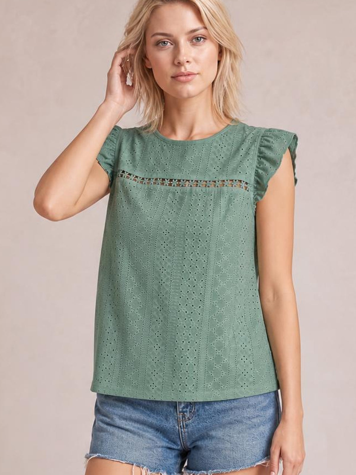 A model poses in a sage green eyelet round-neck top with cap sleeves, a relaxed straight silhouette, and a horizontal cutout panel.