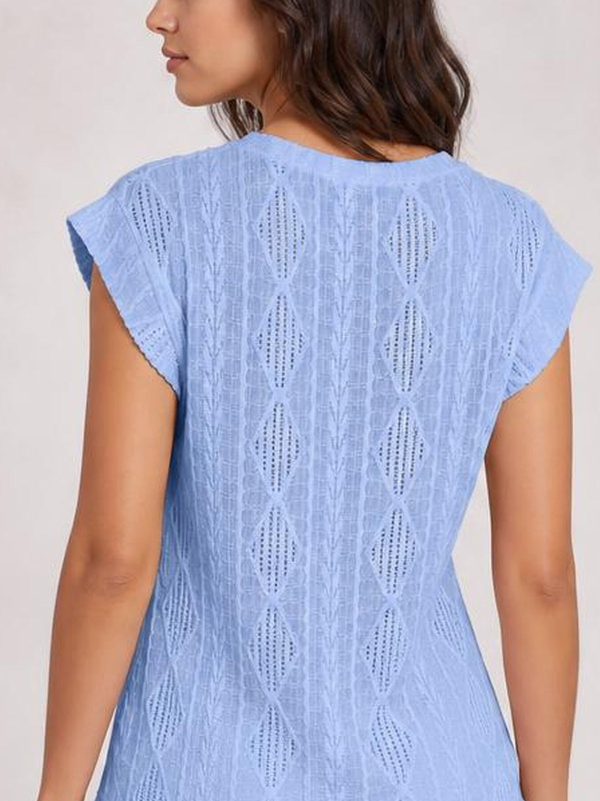 A model shown from the back wears a light blue eyelet top with a round neck, cap sleeves, textured cutout pattern, and a gently fitted silhouette.