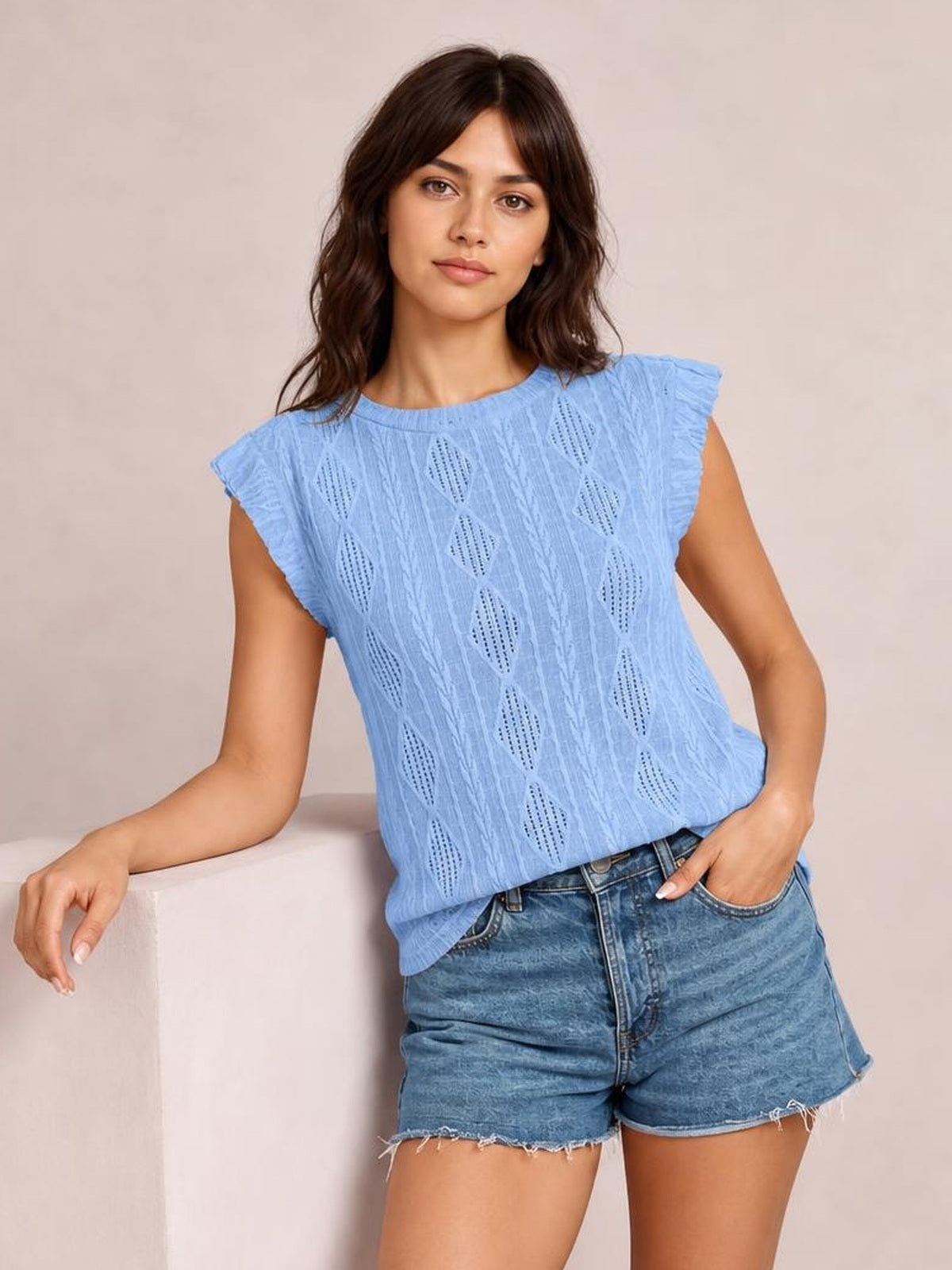 Model wears a light blue eyelet top with a round neckline, ruffled cap sleeves, and a relaxed straight silhouette while posing with one hand in her shorts pocket.