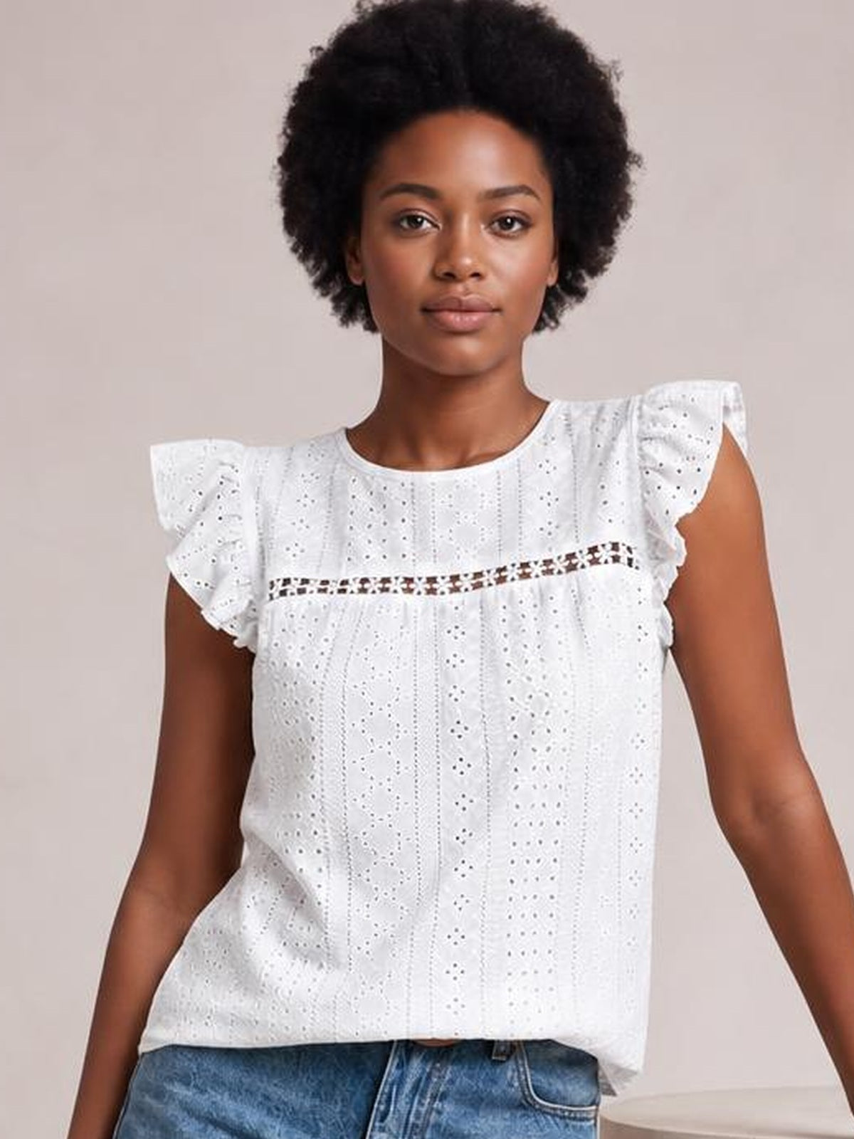 A model faces forward in a white eyelet top with a round neck, fluttering cap sleeves, cutout detailing, and a relaxed straight silhouette.