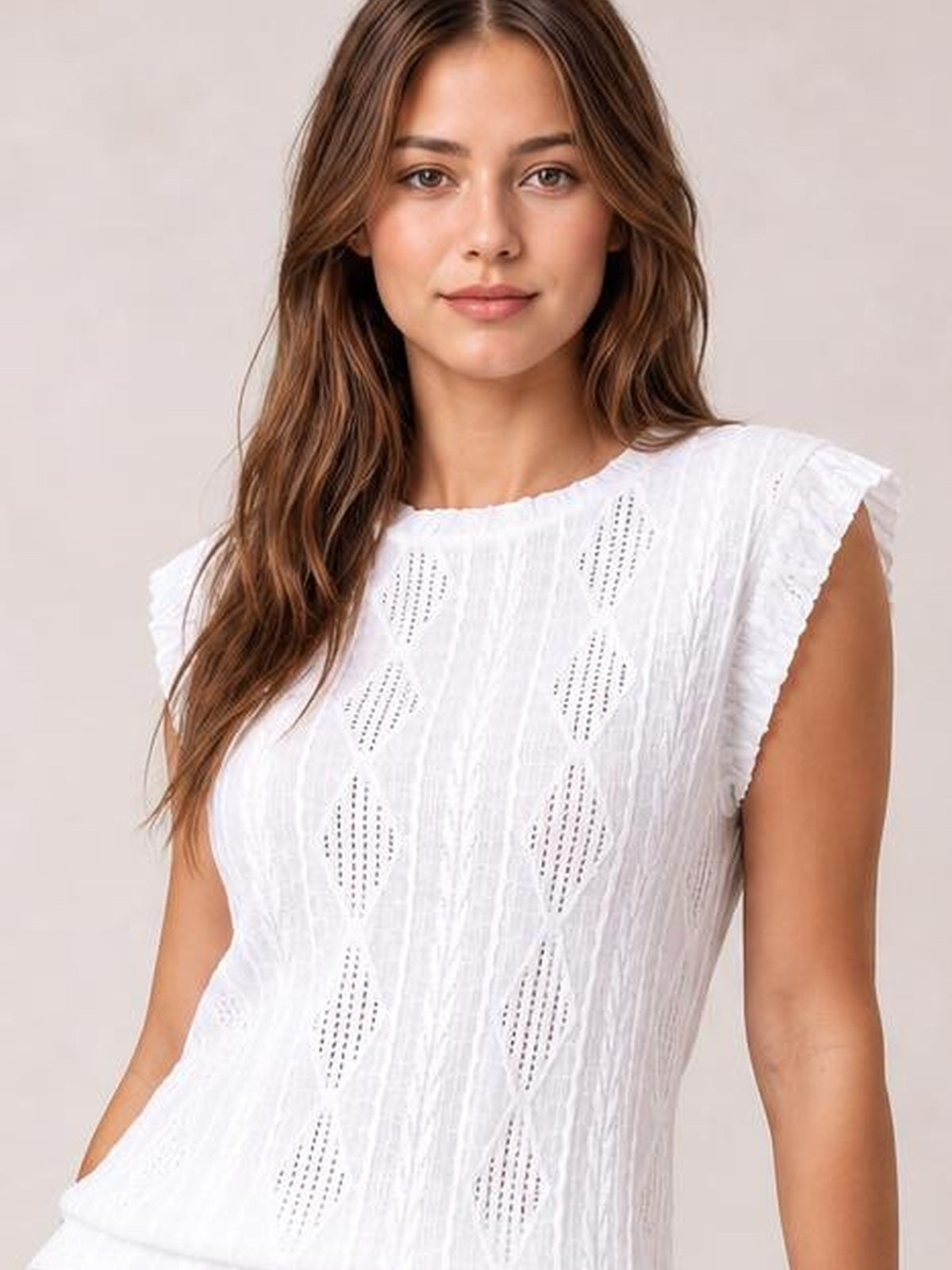 A model wears a white opaque eyelet top with a round neckline, cap sleeves, relaxed silhouette, and vertical cutout detailing.
