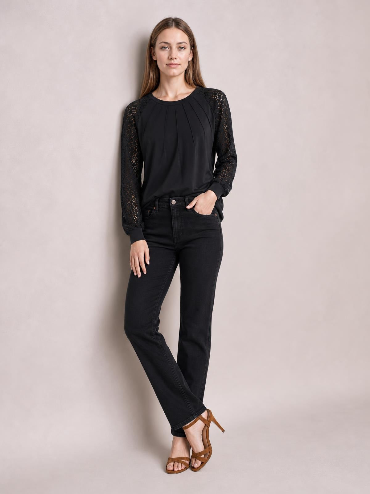 Model poses in a black eyelet round neck long sleeve blouse with semi-sheer sleeves, pleated front, and a relaxed silhouette.