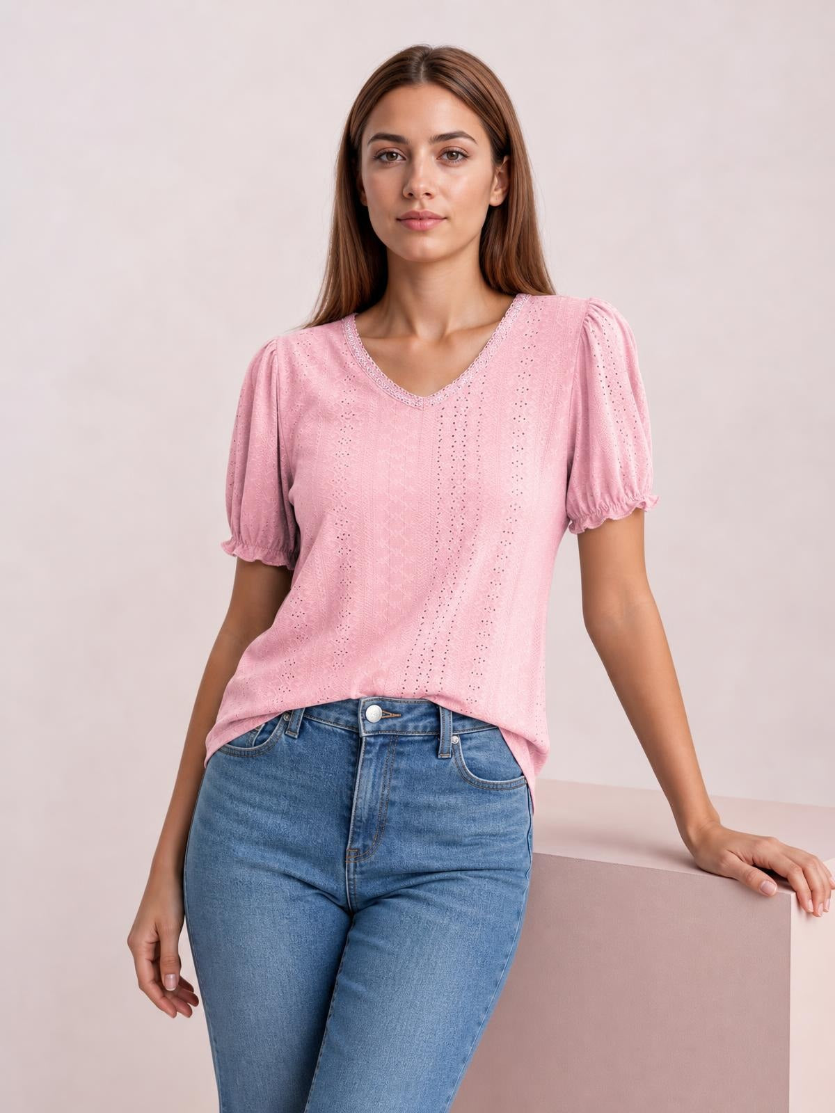 A model wears a pink eyelet blouse with a softly rounded neckline, short puff sleeves with frilled edges, and a relaxed straight silhouette.