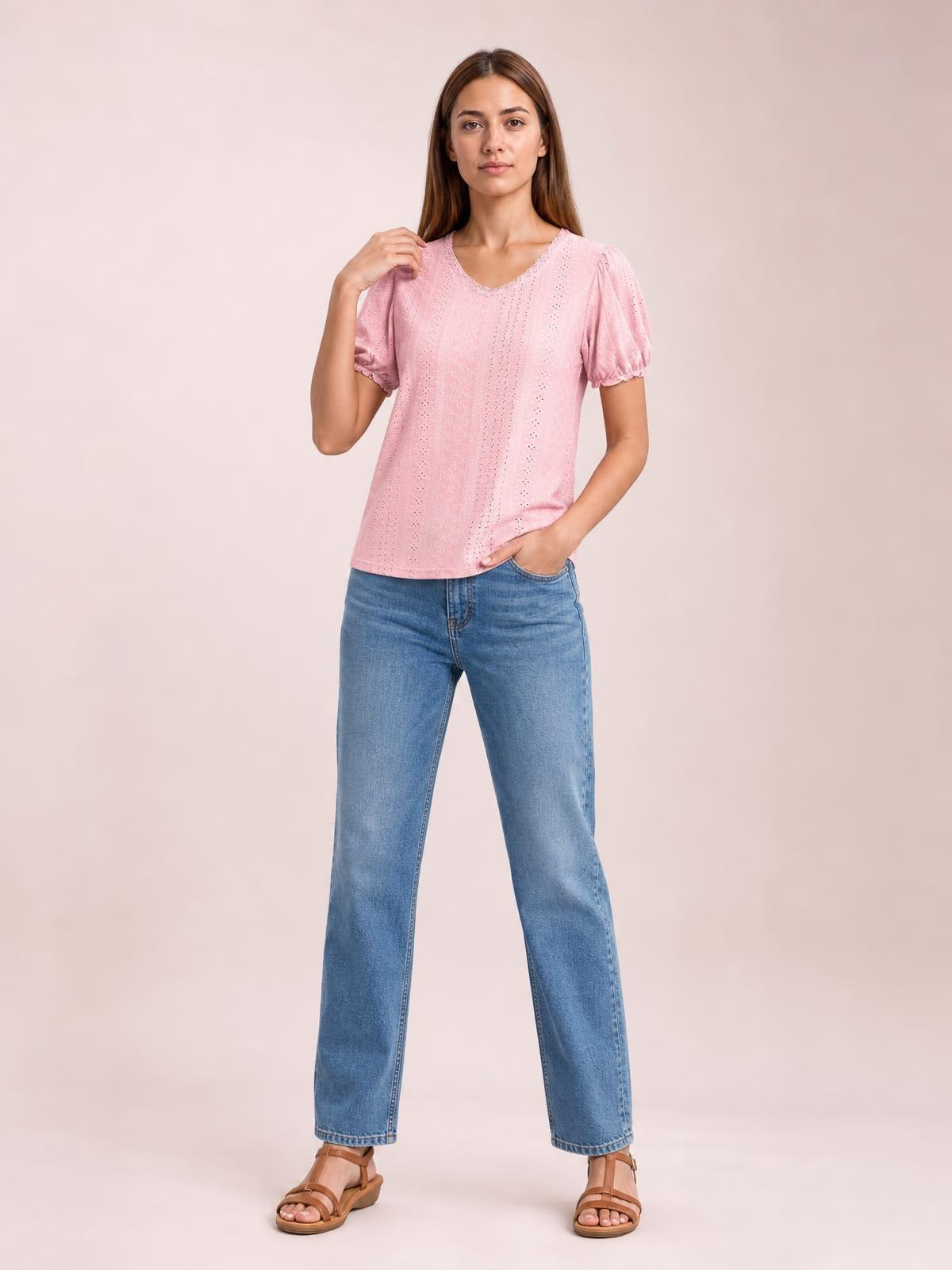 A model wears a pink eyelet round-neck blouse with short puff sleeves, delicate frill trim, and a relaxed straight silhouette, posing with one hand in her jeans pocket.